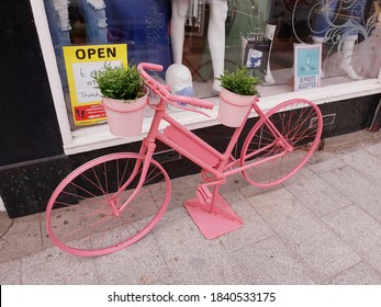 BRAY, CO. WICKLOW, IRELAND - AUGUST 29, 2020: Artificial Plants Stand Made Of Old Bicycle Painted In Pink Color. External Decoration Of Clothing Shop In Bray Town, County Wicklow, Ireland. Usable Art.