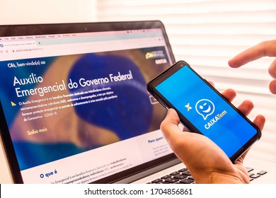 Brazil - April 2020: Hand Holding A Mobile Phone With Caixa Tem App Logo And A Notebook Displaying The Emergency Financial Support From Brazilian Federal Government Due To Covid-19 Pandemic On Screen