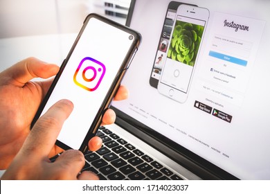 Brazil - April 2020: Hand Holding A Mobile Smart Cell Phone Device With Instagram Social Network App Logo On Screen Over A Notebook With The Log In Instagram Web Page On Display