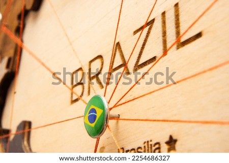 Brazil flag on the pushpin with red thread showed the paths of movement or areas of influence in the global economy on the wooden map. Planning of traveling or logistic concept. Network connection. 