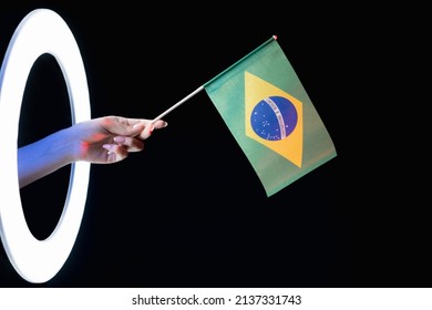 Brazil Flag. Patriotic Identity. Culture Pride. Female Fan Hand Holding Green Yellow Blue National Symbol In LED Light Ring Isolated On Black Background.