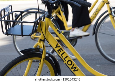 BRASÍLIA, BRAZIL - MAY 5, 2019: Yellow bicycle sharing startup - two bikes closeup frame, with stem, basket and wheels with city public highway and a person's leg and sneakers detail on the background