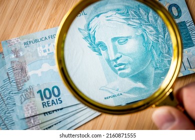 Brazil Money, 100 Reais Banknotes Viewed Through A Magnifying Glass, Financial Business Concept Of The Health Of The Brazilian Economy And The Purchasing Power Of Money