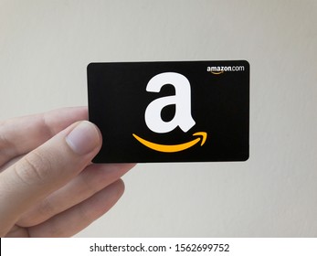 Brazil - November 17, 2019: A young Caucasian male's hand holds an Amazon.com gift card a few weeks before the beginning of the holiday season in front of an off white backdrop.