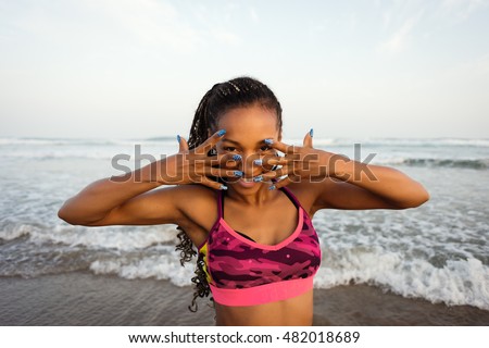 Brazilian black woman dancing and showing fashion decorative nails at the beach.