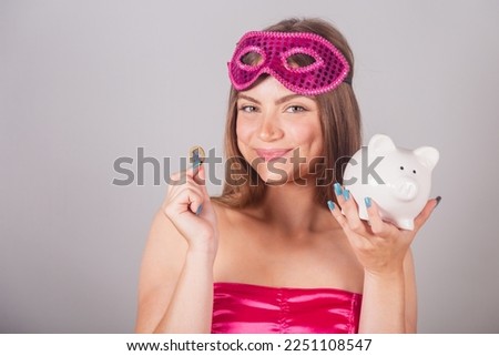Brazilian blonde woman dressed in pink carnival clothes. holding piggy bank and coin. Save money. invest.