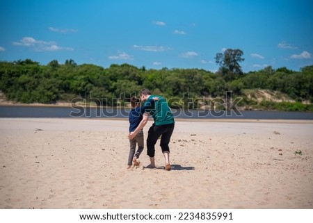 Brazilian boy and adult man walking on the sands of a river beach. Beach on the Santa Maria river in Rio Grande do Sul. People walking on the beach. Sand and fresh water. People and lifestyle.