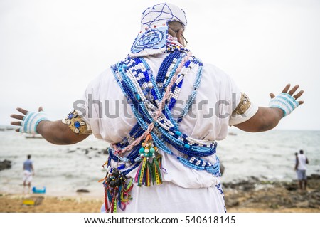 A Brazilian candomble priest performs a blessing at the Festival of Yemanja in traditional blue and white robes with colorful beads on the beach at Rio Vermelho in Salvador, Bahia, Brazil