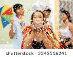 Brazilian Carnival. Group of friends celebrating carnival party. Selective focus of woman blowing confetti.
