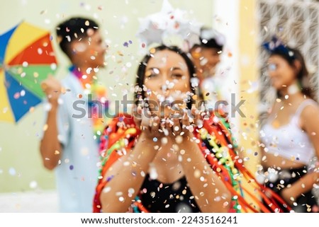 Brazilian Carnival. Group of friends celebrating carnival party. Selective focus of woman blowing confetti.