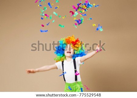 Brazilian Carnival. Happy clown boy with large colorful wig. Let's party! Funny kid clown. 1 April Fool's day concept. Portrait of a child throws up a multi-colored tinsel and confetti. Birthday boy.