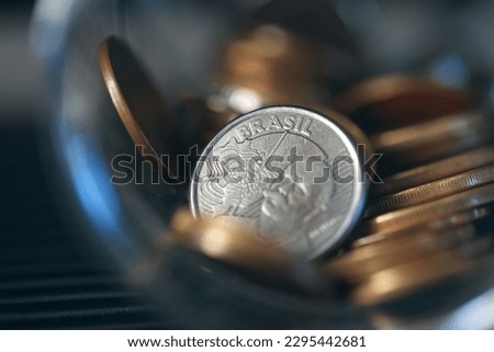 Brazilian coins inside a glass jar. Highlight for 50 cents coin. Brazilian economy. Dark environment. Macro photography.