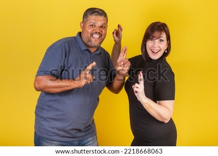 Brazilian couple, Caucasian woman and black man, fingers crossed, cheering, wishing you a lot of luck sign.