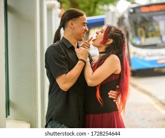 Brazilian Couple Holding Each Other On The Street With Blurred Background, The Girl Has Red Hair, And The Boy Has Long Hair. Dia Dos Namorados.