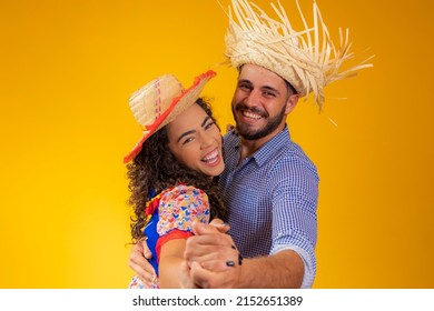 Brazilian couple wearing traditional clothes for Festa Junina dancing on yellow background