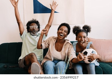 Brazilian family celebrating and watching a football game together. Parents and their daughter sitting on the couch, smiling with excitement. Happy black family of soccer fans. - Powered by Shutterstock