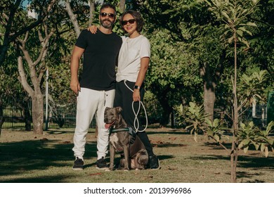 Brazilian Family Formed By Man, Woman And A Pit Bull Dog In The Public Park. Affection And Love Relationship Between Humans And Animals.