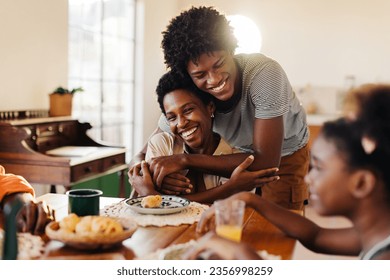 Brazilian family having breakfast, with mom and son sharing hugs at their kitchen table. Happy black family enjoying quality time together, with fresh cheese bread rolls served on the table. - Powered by Shutterstock