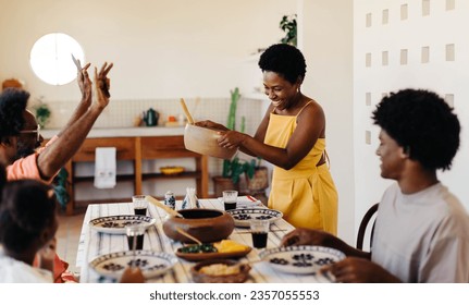 Brazilian family having a traditional meal together. Mom serving food from a clay pot while the children await their servings. The kitchen is filled with the aroma of black beans, farofa, and couve. - Powered by Shutterstock