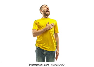 Brazilian fan celebrating on white background. The young man in soccer football uniform standing and singing a hymn at white studio. Fan, support concept. Human emotions concept.