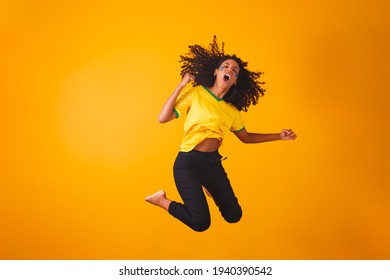 Brazilian fan. Jumping to celebrate, Brazilian fan celebrating football or soccer game on yellow background. Colors of Brazil. - Shutterstock ID 1940390542