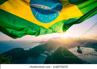 Brazilian Flag Shines Above The Golden Sunset City Skyline At Sugarloaf Pao De Acucar Mountain In Rio De Janeiro. Translation: Order And Progress