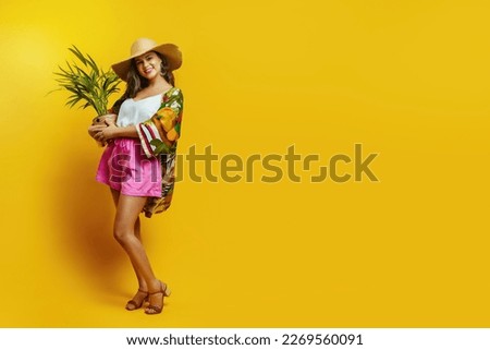 A Brazilian girl in a hat and bright clothes holds a small palm tree in a pot in her hands.