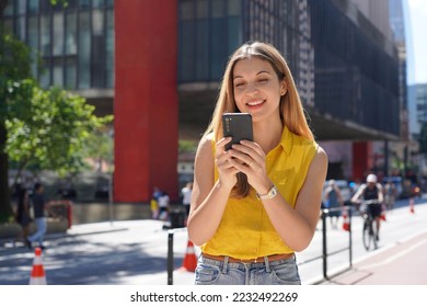 Brazilian girl using mobile phone app for chat on sunny day in Paulista Avenue, Sao Paulo, Brazil