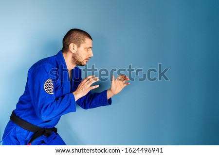 Brazilian jiu jitsu bjj caucasian athlete instructor professor or fighter standing in front of the blue wall wearing kimono gi uniform side view in fighting stance