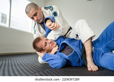 Brazilian jiu jitsu bjj training or sparing two athletes fighters dill martial arts technique at gym on the tatami mats wear kimono gi black belt instructor demonstrate submission choke
