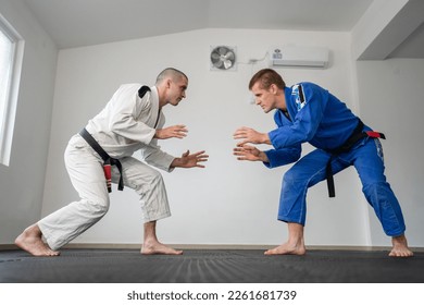 Brazilian jiu jitsu bjj training or sparing two athletes fighters dill martial arts technique at gym on the tatami mats wear kimono gi black belt instructor demonstrate technique stand up