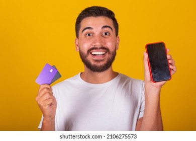 Brazilian Latin American Man, Surprised And Happy, Showing Cellphone Screen And Credit Card, Mobile Phone Shopping, App, Internet Shopping Concept.