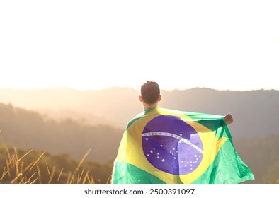 Brazilian man with the Brazilian flag on his back and arm raised to express national pride and celebration of Brazil's Independence Day. In the background there is a sunset in the mountains - Powered by Shutterstock