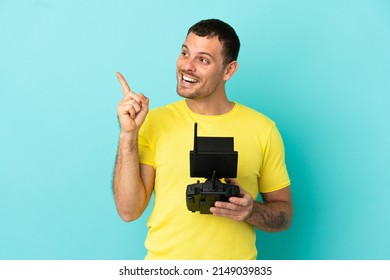 Brazilian man holding a drone remote control over isolated blue background intending to realizes the solution while lifting a finger up