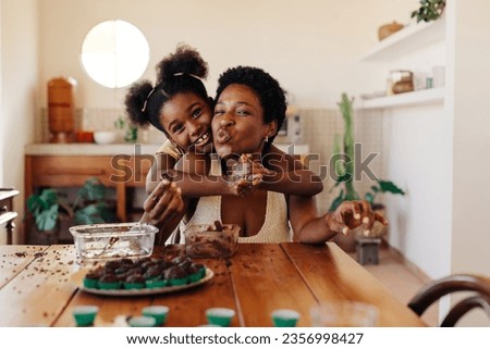 Brazilian mom and daughter making brigadeiro in the kitchen. Mother and daughter enjoy preparing chocolate fudge balls for dessert, creating a happy moment of teaching and learning traditional recipes