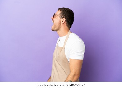 Brazilian Restaurant Waiter Over Isolated Purple Background Laughing In Lateral Position