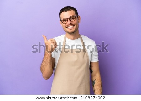 Brazilian restaurant waiter over isolated purple background pointing to the side to present a product