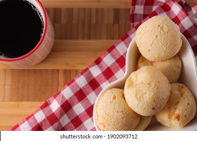 Brazilian snack cheese bread in a heart shaped bowl and coffee" Pao de queijo" in a wooden background.  Small bacon cheese rolls. Also known in Latin America as Chipa, Pan de Bono and Pan de Yuca. 