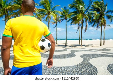 Brazilian soccer player holding football wears shirt in Brazil colors at Copacabana beach, Rio de Janeiro