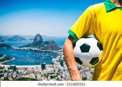 Brazilian Soccer Player Holding Football Wearing Shirt In Brazil Colors At Rio De Janeiro Skyline With Sugarloaf Mountain