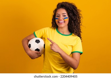 Brazilian supporter. Brazilian woman fan celebrating on soccer or football match on yellow background. Brazil colors.Pointing 