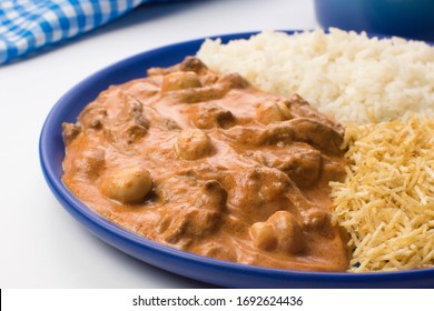 Brazilian tenderloin stroganoff with rice and potato sticks in a blue plate in white background close