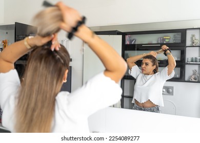 Brazilian woman combing hair, do hairstyle in bathroom with hairbrush and band. Female morning routine. Soft focus - Powered by Shutterstock