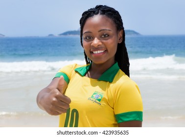 Brazilian Woman In A Soccer Jersey At Beach Showing Thumb Outdoor At Beach With Ocean And Blue Sky In The Background