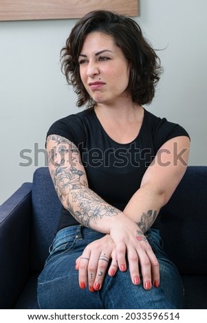 Brazilian woman, tattooed, with her hands crossed and looking to the side, showing contempt.