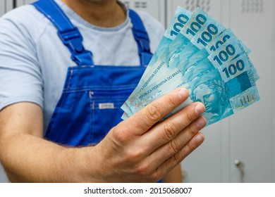 Brazilian Worker Showing Money. Bundle Of Banknotes, Concept, Salaries Of Professionals And Blue Collar Workers