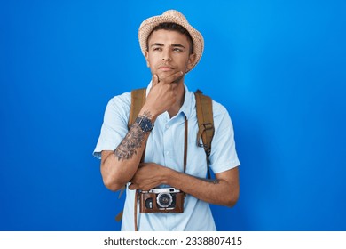 Brazilian young man holding vintage camera looking confident at the camera with smile with crossed arms and hand raised on chin. thinking positive.  - Powered by Shutterstock