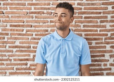 Brazilian young man standing over brick wall smiling looking to the side and staring away thinking.  - Shutterstock ID 2302125211