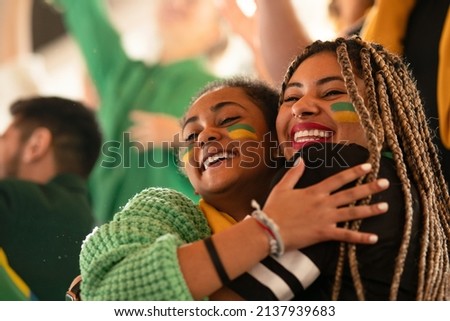 Brazilian young sisters football fans celebrating their team's victory at stadium.