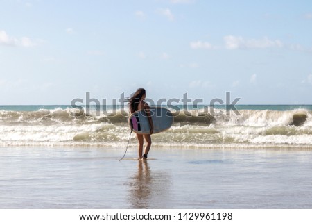 A Brazilian young woman walking on beach with surfboard at Natal, Brazil.